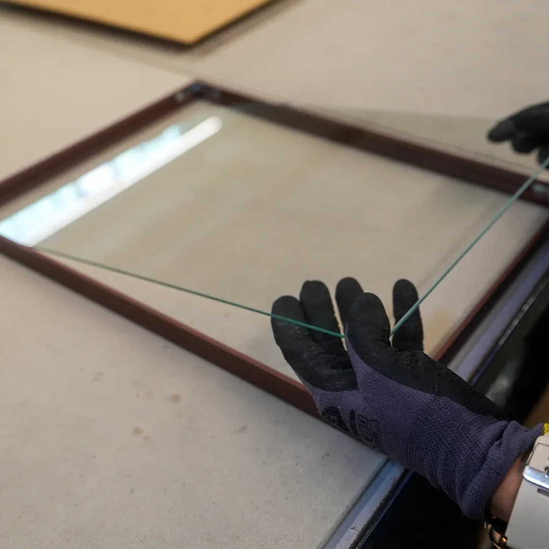 Con guantes de protección se coloca un cristal en un marco de madera oscuro