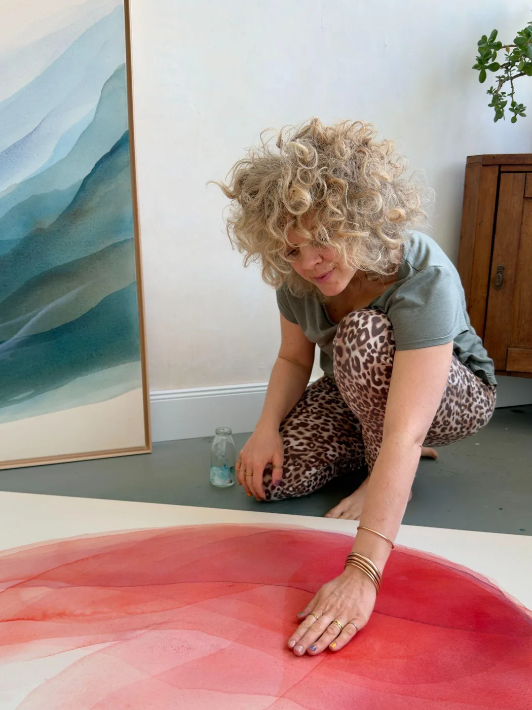 Johanne Bossmann pinta con la mano sobre un lienzo en tonos rojos, junto a una obra azul enmarcada