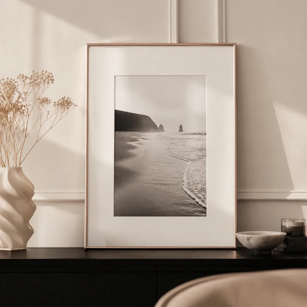 Marco de plástico blanco con foto de playa en blanco y negro y paspartú sobre una cómoda