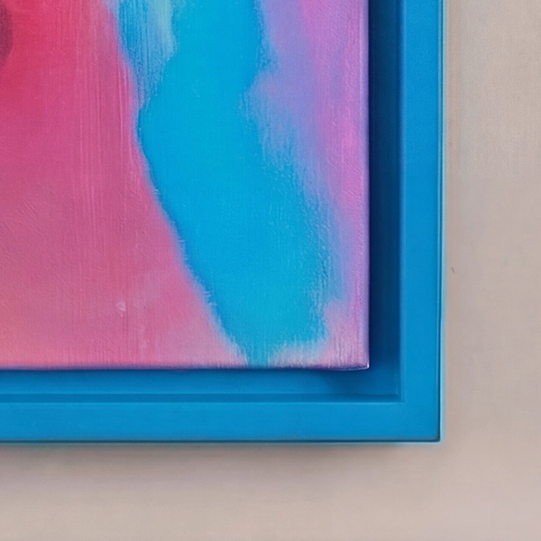 Primer plano de un marco de caja americana azul con un lienzo colorido en rosa y turquesa, sobre una pared de color beige claro.