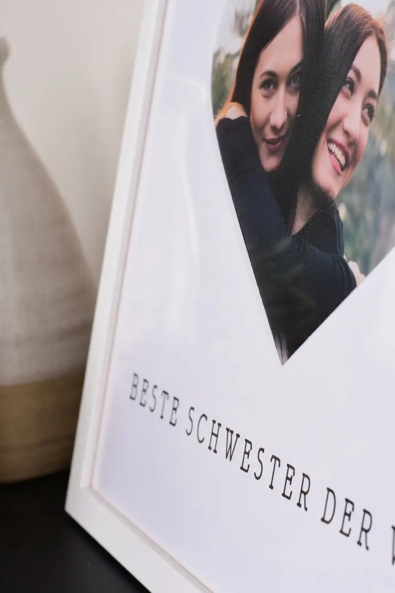 Primer plano de un marco de fotos de 30x30 en blanco con un recorte en forma de corazón para la mejor hermana del mundo.